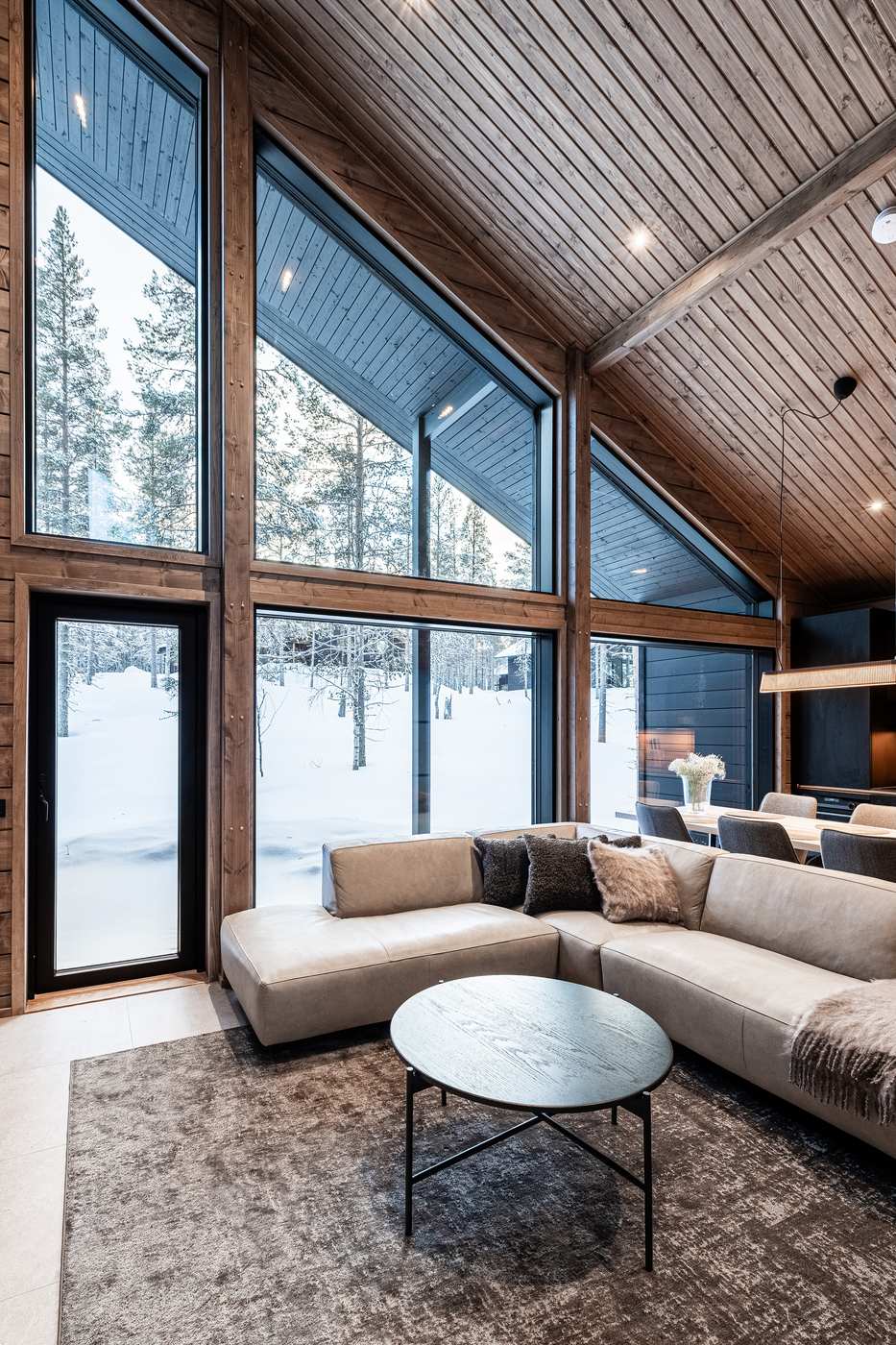 Living room with tall windows, leather corner sofa and view of the snowy forest
