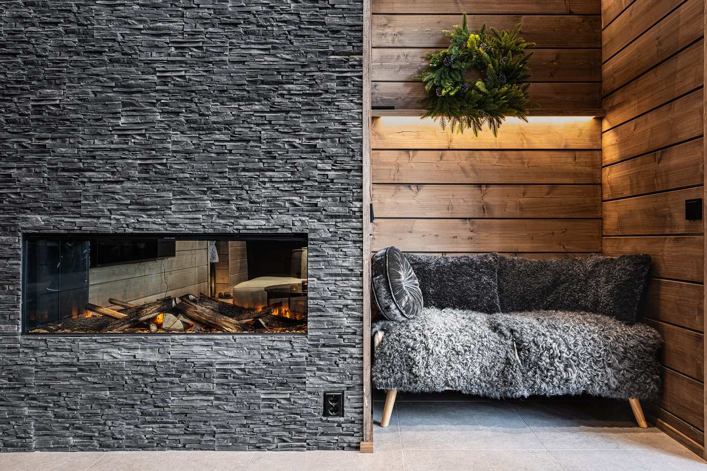 Fireplace in a dark stone wall beside a seating nook with sheepskin