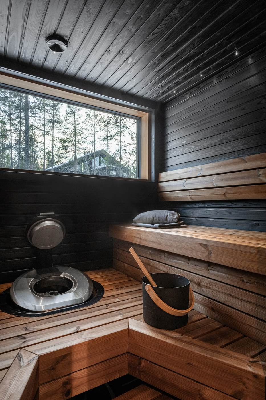 Sauna in dark timber with tiered benches and a window to the forest