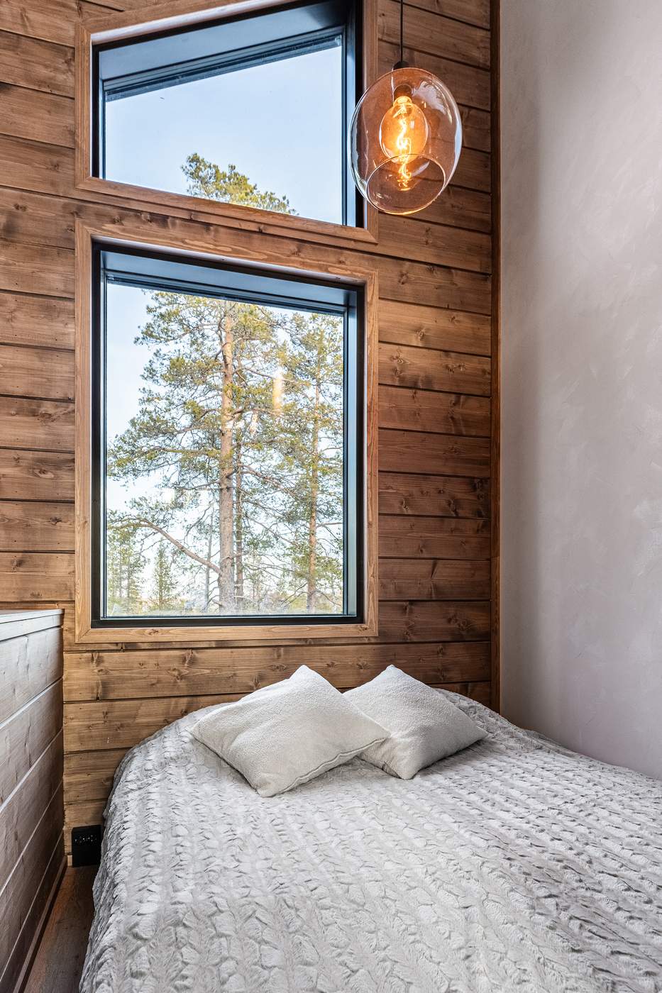 Bedroom with pendant light and tall window onto the pines